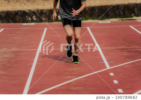 陸上競技場のトラックを走る男性ランナー 100789682
