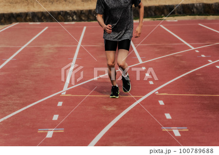 陸上競技場のトラックでスタートダッシュする男性ランナー 100789688