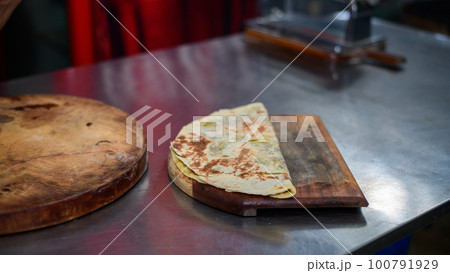 Crunchy folded single tortilla bread on a wooden plate on the kitchen table. 100791929