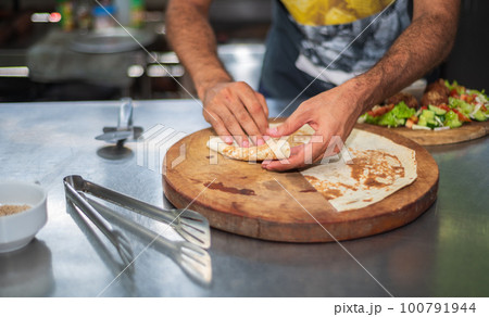 A chef prepares a falafel plate and tortillas on a round wooden cutting board in the kitchen. A chef prepares a falafel plate and tortillas on a round wooden cutting board in the kitchen. 100791944