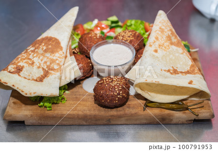 Presenting the middle eastern Lebanese dish Falafel on a wooden plate. tortilla, vegetable salad, and tahini sauce. Presenting the middle eastern Lebanese dish Falafel on a wooden plate. tortilla, vegetable salad, and tahini sauce. 100791953