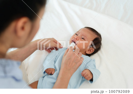 mother using finger to clean newborn baby mouth (tongue and gum) with clean gauze on bed mother using finger to clean newborn baby mouth (tongue and gum) with clean gauze on bed 100792089