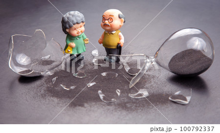 miniature people. a couple of elderly people near a broken hourglass. miniature people. a couple of elderly people near a broken hourglass. 100792337