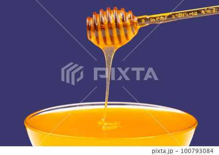 fresh fragrant honey drips from a spoon into a plate on a colored background. fresh fragrant honey drips from a spoon into a plate on a colored background. 100793084