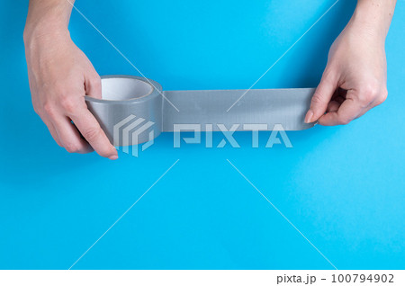 Woman holding silver scotch tape on blue background. Woman holding silver scotch tape on blue background. 100794902