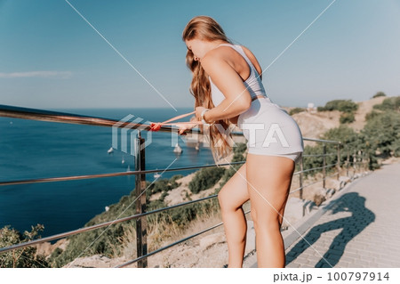 Fitness woman sea. Outdoor workout with fitness rubber bands in park over beach. Female fitness yoga routine concept. Healthy lifestyle. Happy fit woman exercising with rubber band in park. Fitness woman sea. Outdoor workout with fitness rubber bands in park over beach. Female fitness yoga routine concept. Healthy lifestyle. Happy fit woman exercising with rubber band in park. 100797914