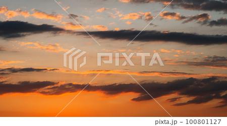 A fabulously beautiful summer sunset. Dark clouds in yellow and orange colours. The sun's rays from below illuminate the clouds. The beauty of nature. 100801127