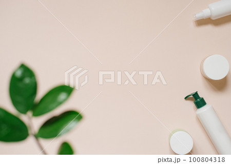 White cosmetic jar and a bottle of cream with a top view of the leaves of plants, a mock-up of the product design. Natural organic cosmetics 100804318
