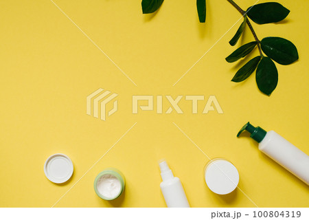 Set of organic SPA cosmetics with green leaves. Top view of bottles made of white recyclable plastic on a yellow background with a copy space. Packaging design of natural cosmetic products for skin 100804319