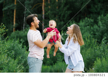 Happy young parents with a baby are walking through the forest, having fun and enjoying happy moments 100804321
