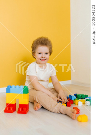 Child is playing with colorful cubes at the table. Kid has fun and builds from bright construction blocks. Early learning. Educational toys 100804323