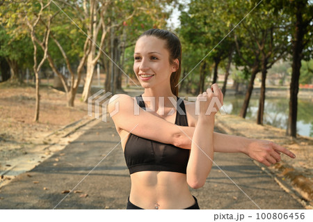 Healthy sports woman stretching her arms, warm up before workout in the park. Fitness, training and healthy lifestyle concept 100806456