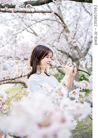 満開の桜の写真を撮る若い女性 100807062