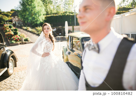 Wedding bride and groom, elegant couple staying near retro wedding car 100810482