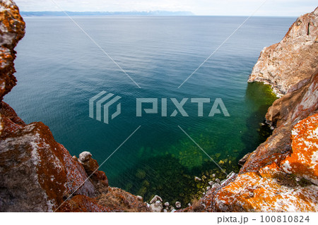 View of Lake Baikal with green transparent water from a cliff. The rock is covered with red moss. Sunny. View of Lake Baikal with green transparent water from a cliff. The rock is covered with red moss. Sunny. 100810824