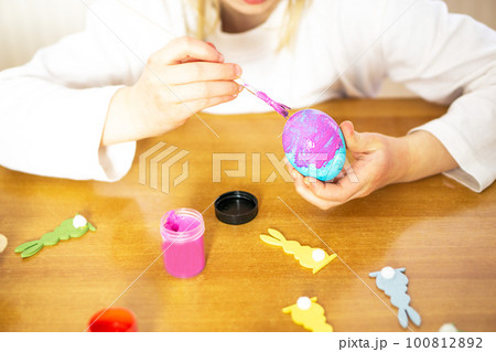 Child hands painting eggs for Easter on the wooden table at home. Preparation for Easter celebration 100812892