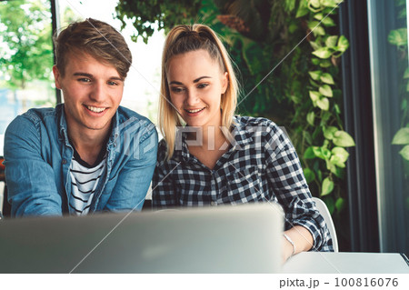 Smiling young couple sitting at a caffe, paying their apartment bills on the laptop  100816076