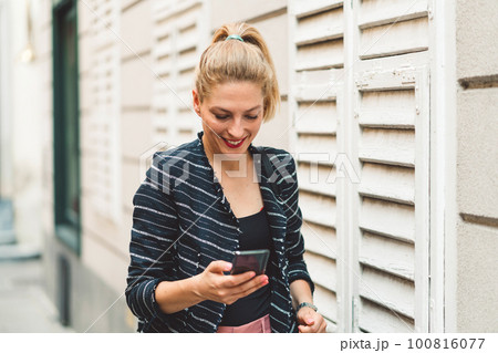 Woman running errands in the city, waist up looking at her phone while walking fast to a meeting  100816077
