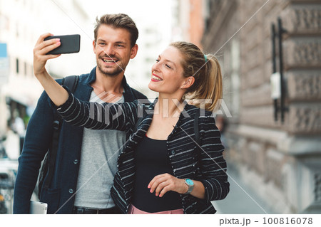 Smiling woman holding a phone taking a selfie of herself and her boyfriend  100816078