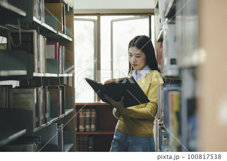Student standing and reading book at library. Student standing and reading book at library. 100817538