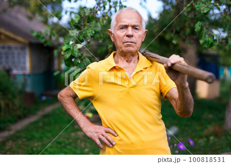 Old man standing in backyard with shovel in hand 100818531