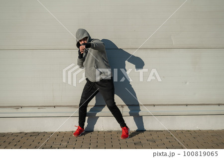 A man in a hoody trains boxing against a gray wall.  100819065