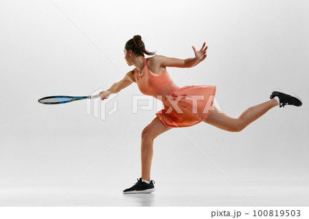 Serving ball, start of game. Portrait of young woman, professional female tennis player in uniform training against white studio background. Serving ball, start of game. Portrait of young woman, professional female tennis player in uniform training against white studio background. 100819503
