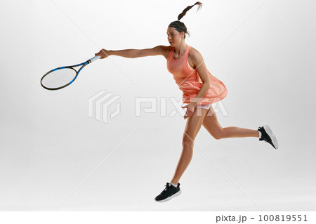 Portrait of young sportive woman, professional female tennis player in uniform training against white studio background. In motion 100819551