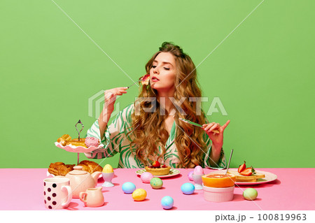 One pretty girl having family holiday dinner with manner face expression over green background. Colorful eggs on table 100819963