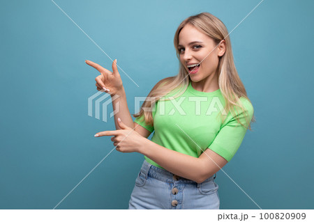 energetic girl in casual outfit pointing at the wall on the left on a blue background energetic girl in casual outfit pointing at the wall on the left on a blue background 100820909