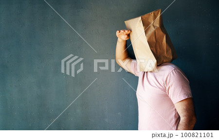 Man with a paper bag on head looking far away distance over gray background 100821101