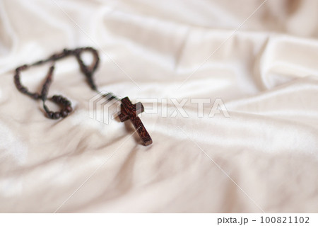 A wooden rosary with crucifix isolated on a beige colored fabric background to represent and symbolize lent, solemn Christian religious observance  100821102