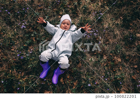 Little girl in violet boots and blue overall lying in spring blooming forest Little girl in violet boots and blue overall lying in spring blooming forest 100822201