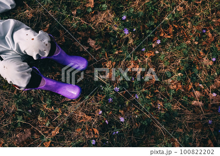 Unrecognizable little girl in violet boots and blue overall lying in spring blooming forest 100822202