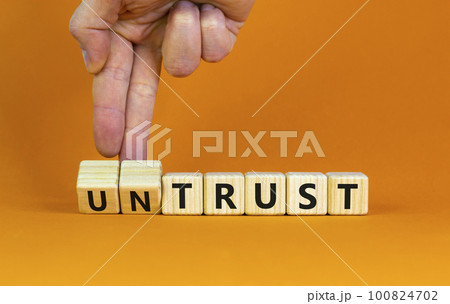 Untrust or trust symbol. Businessman turns wooden cubes, changes words 'untrust' to 'trust'. Beautiful orange table, orange background. Business and untrust or trust concept, copy space. Untrust or trust symbol. Businessman turns wooden cubes, changes words 'untrust' to 'trust'. Beautiful orange table, orange background. Business and untrust or trust concept, copy space. 100824702