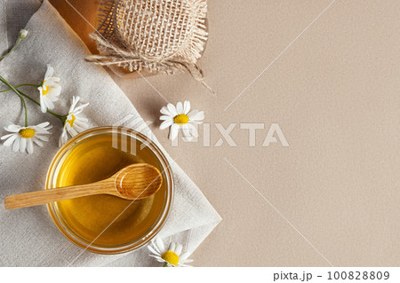 Chamomile syrup in a small bowl and in a jar and chamomile flowers on a linen kitchen towel, topview, copy space 100828809