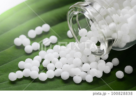 Homeopathic pills scattered from a bottle on a green leaf, close up Homeopathic pills scattered from a bottle on a green leaf, close up 100828838