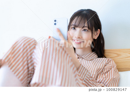 ベッドでスマホを使うパジャマの若い女性 100829147