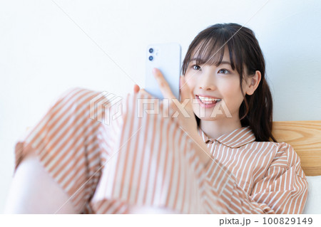 ベッドでスマホを使うパジャマの若い女性 100829149