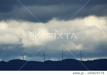 雲の多い午後の空と山の稜線に並ぶ風力発電の風車・春・望遠・230318pm 100829778