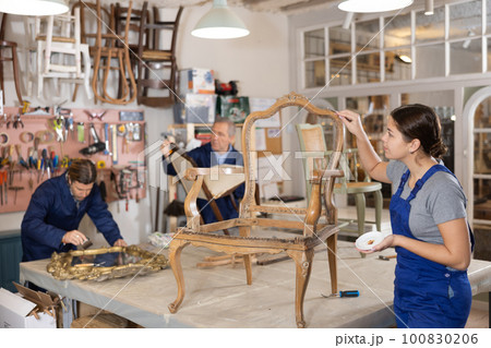 Professional craftswoman restorer in uniform renewing old-fashioned chair while working in repair shop 100830206