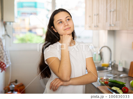 Portrait of confused young woman at kitchen 100830333