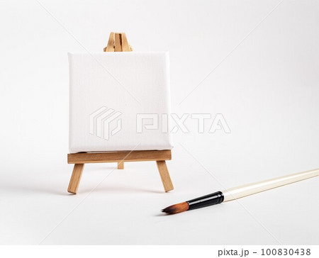 Square canvas on tiny mini easel, blank mockup on wood tripod, paintbrush. Artistic supplies composition. High quality photo Square canvas on tiny mini easel, blank mockup on wood tripod, paintbrush. Artistic supplies composition. High quality photo 100830438