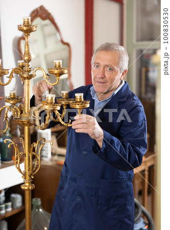 Senior restorer with brush removes dirt and dust deposits from bedside antique floor lamp 100830530