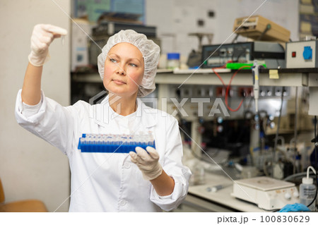 Female lab technician working with reagents in test tubes during chemical experiment 100830629