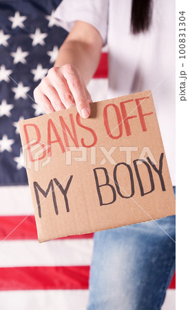 Woman holding a sign Bans Off My Body American flag on background. Protest against anti abortion law. Women's strike. Womens rights freedom. 100831304