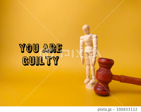 Wooden mannequin and gavel with the word YOU ARE GUILTY on yellow background. Wooden mannequin and gavel with the word YOU ARE GUILTY on yellow background. 100833112
