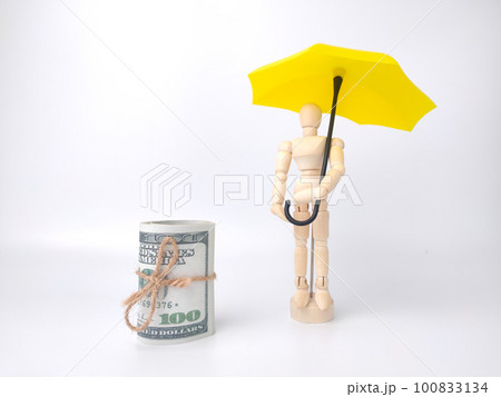 Wooden mannequin holding yellow umbrella and banknotes on a white background. Business concept. 100833134