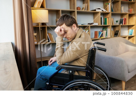 A young handsome man in a wheelchair looks out the window with a sad look 100844830