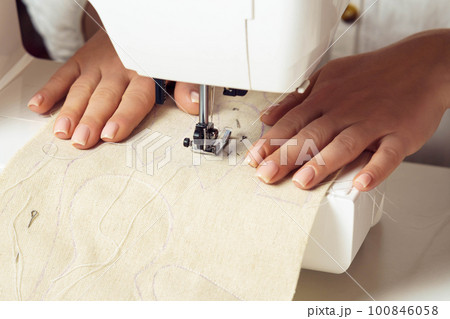Unrecognizable female tailor hands put white fabric textile pattern with stitch contour on sewing machine needle plate 100846058